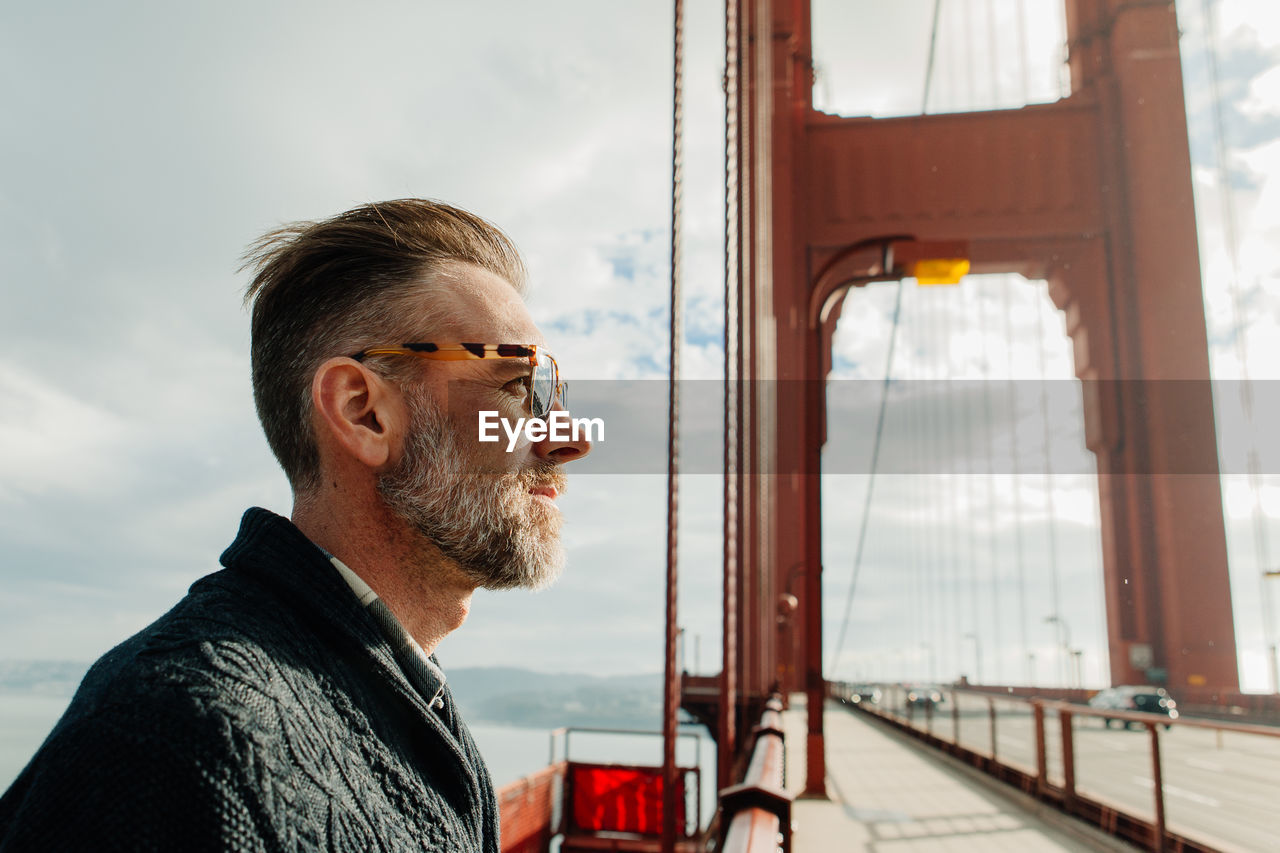 Profile portrait of adult man with beard standing on the golden gate bridge during cloudy weather