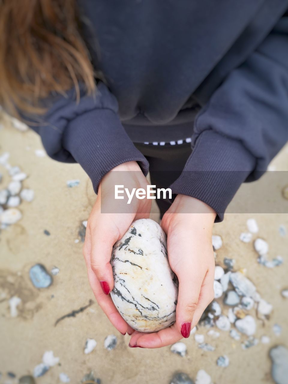 Midsection of woman holding pebble stone at beach