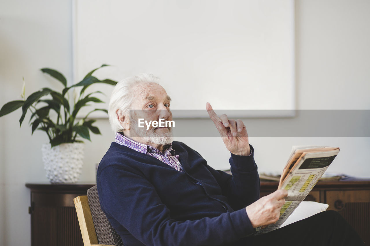 Senior man pointing while holding newspaper in nursing home