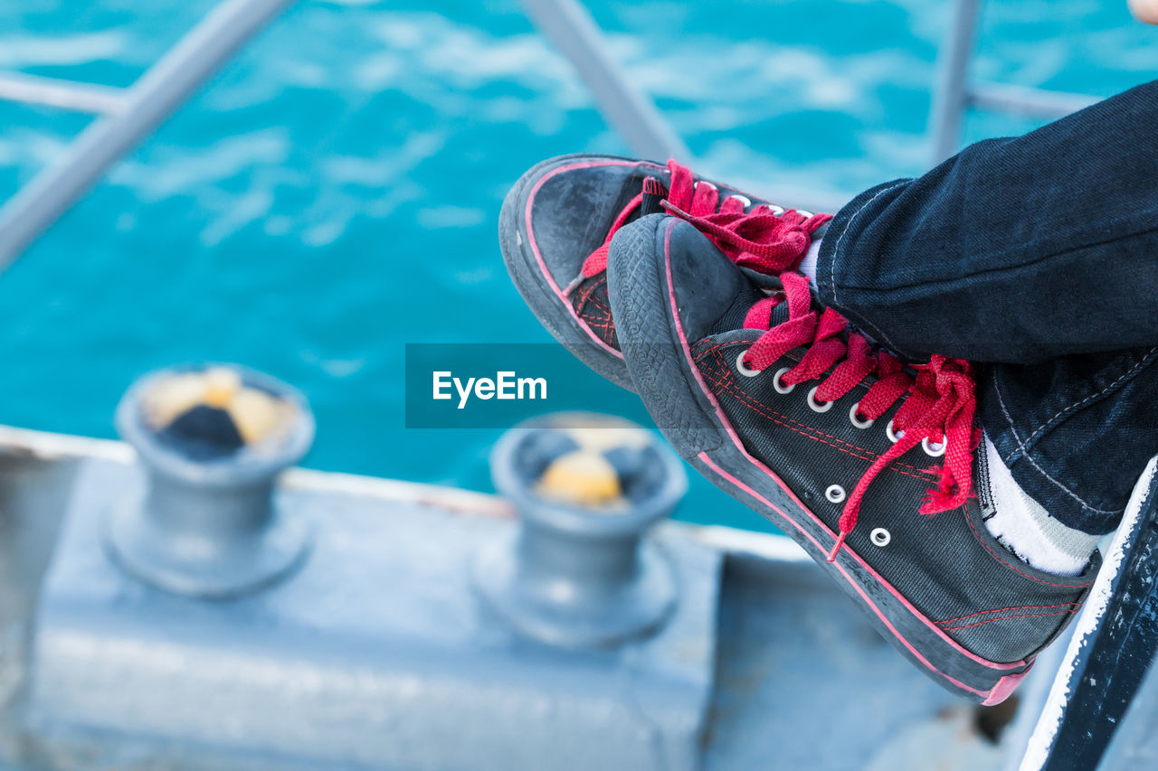 Close-up of person wearing black canvas shoes against blue sea at harbor