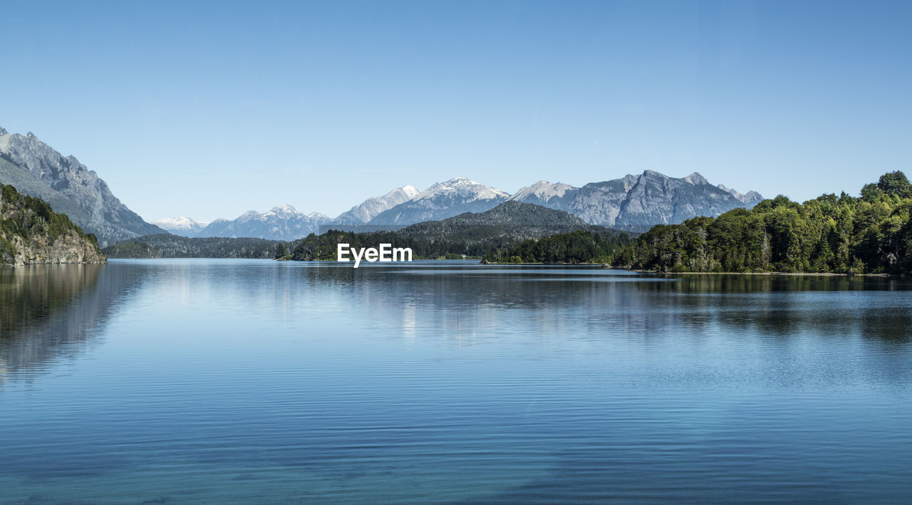 Scenic view of lake and mountains against clear blue sky