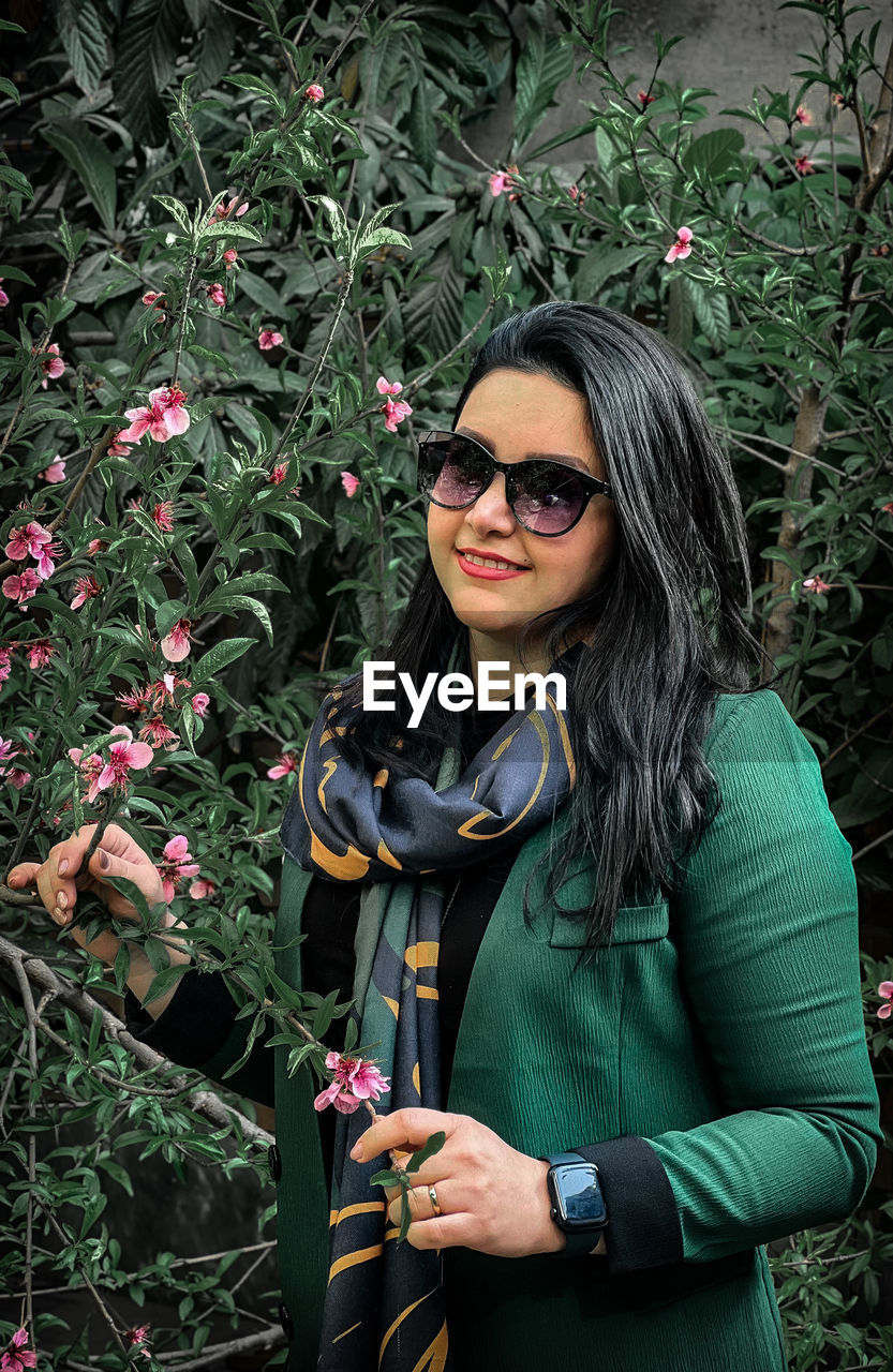 portrait of young woman wearing sunglasses while standing by plants