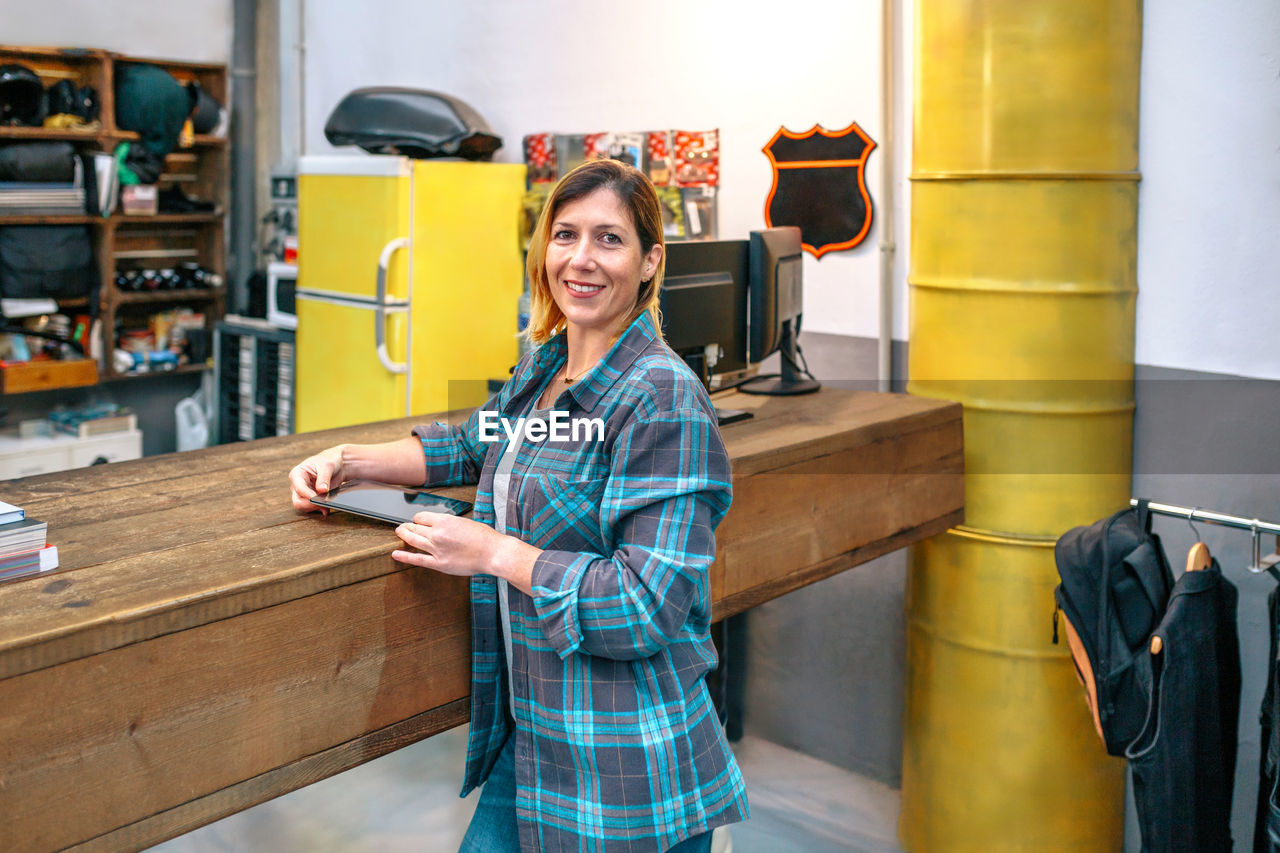 Portrait of happy young woman owner standing in front of store counter with copy space