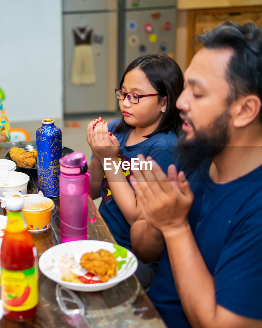Father and daughter praying before eating food at home