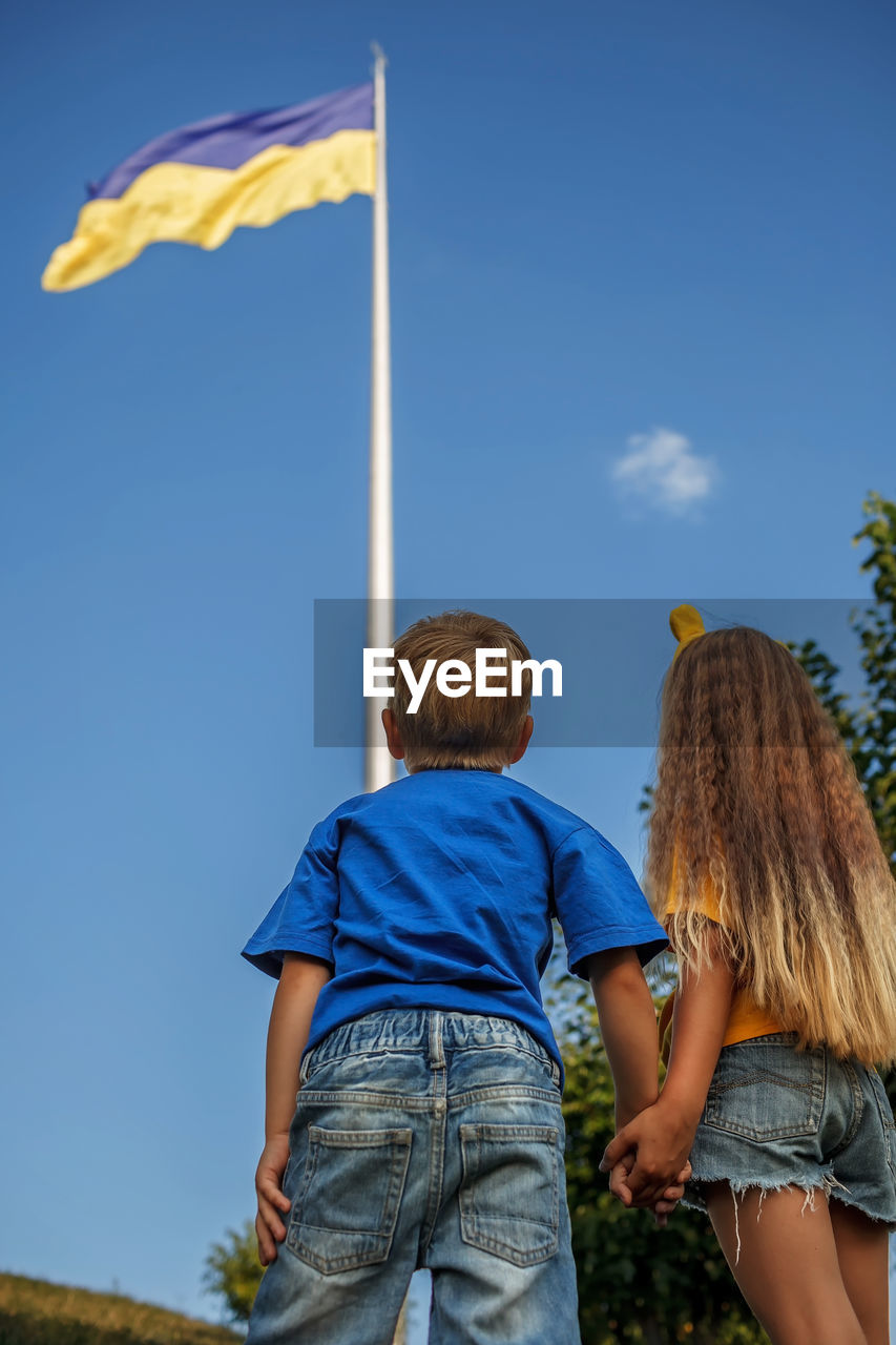 Girl in yellow and boy in blue look at biggest national flag of ukraine. pray for peace and victory