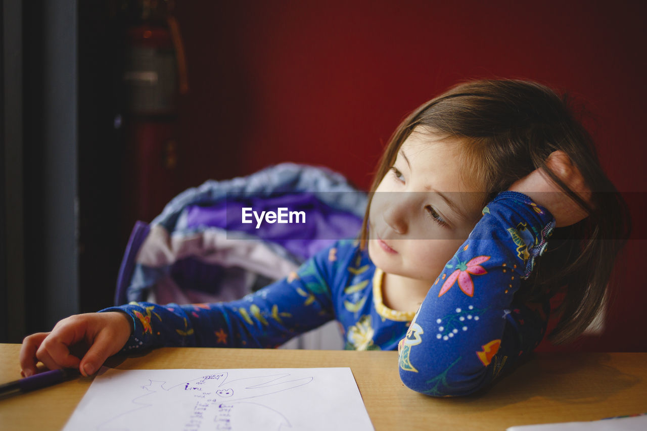 A little girl with drawing paper and pen startes out window dreamily