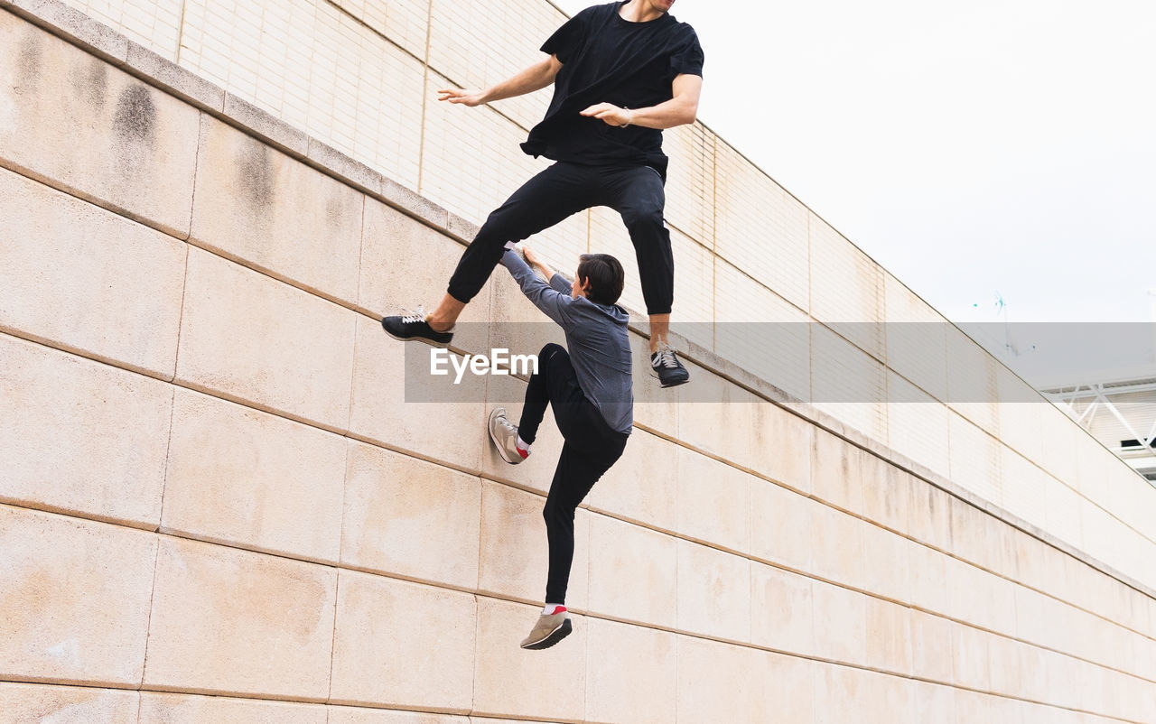 Low angle of anonymous men athlete in sports outfit jumping on wall and pushing off it during training near building