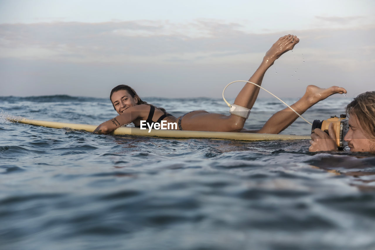 Happy couple with surfboard and camera in ocean