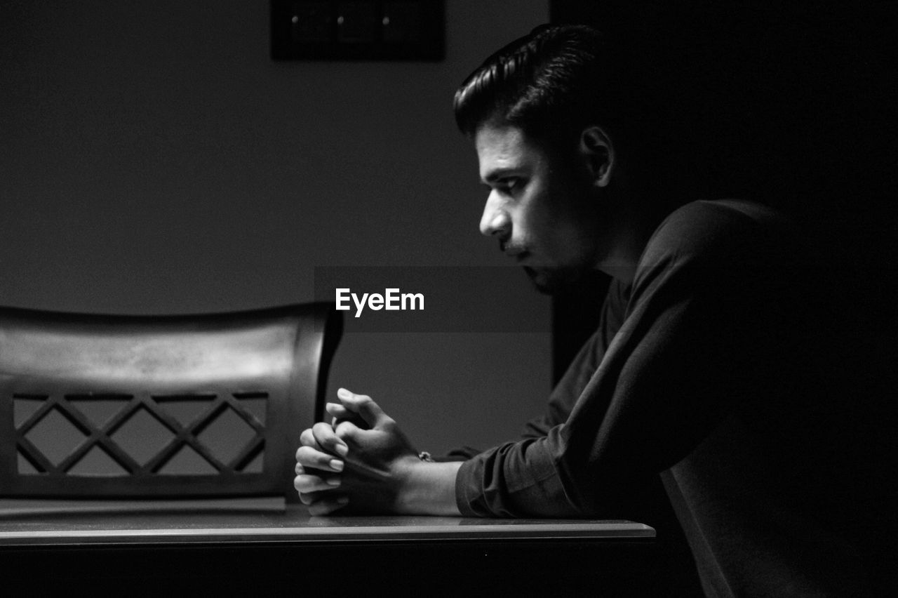 Side view of thoughtful man sitting at table in room