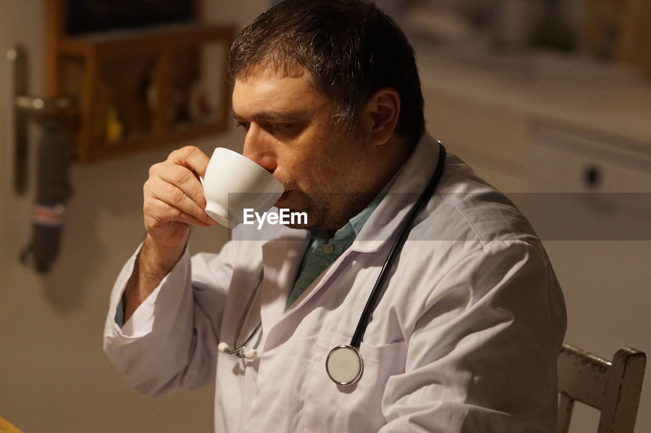 Side view of thoughtful mature doctor drinking coffee sitting in hospital