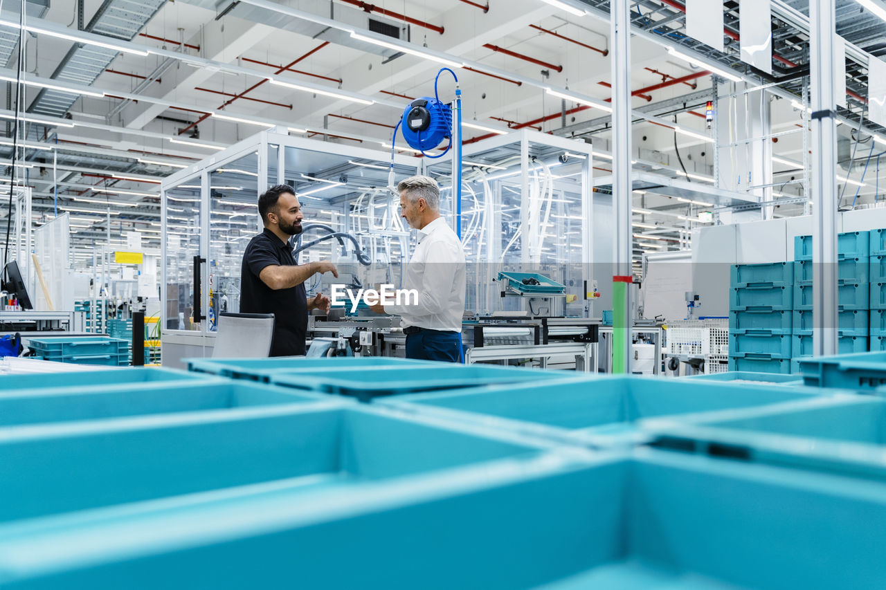 Coworkers having discussion by blue crates at factory production line