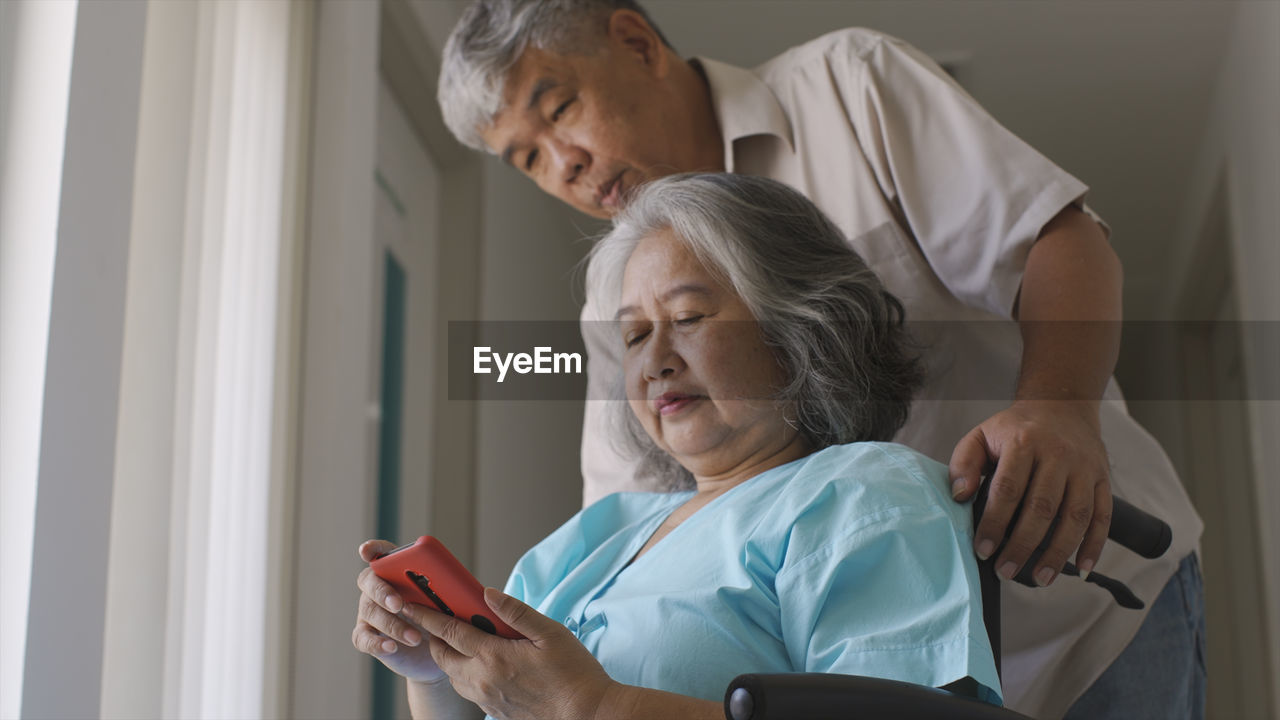 A senior woman and her husband making a video call on a mobile phone in the hospital