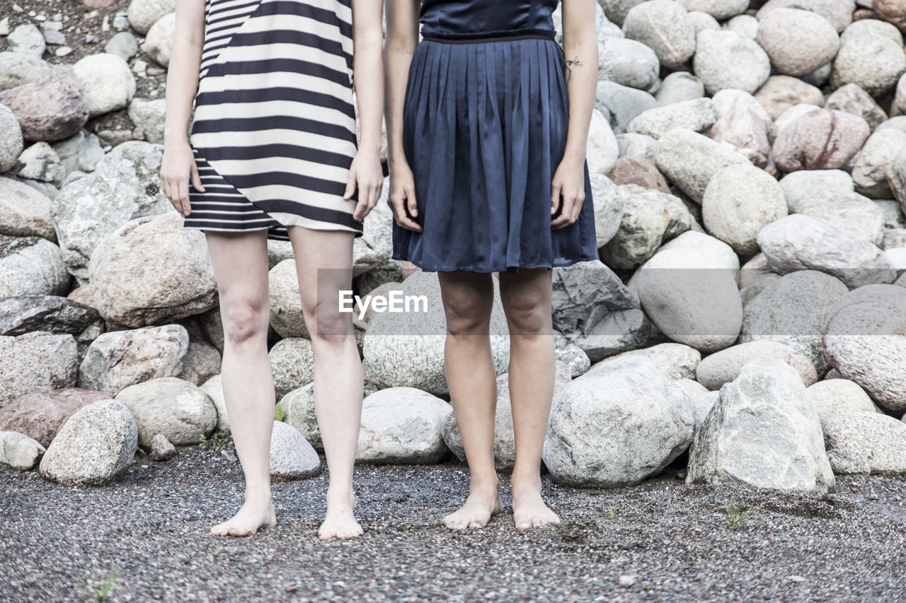 Low section of women standing by rocks at beach