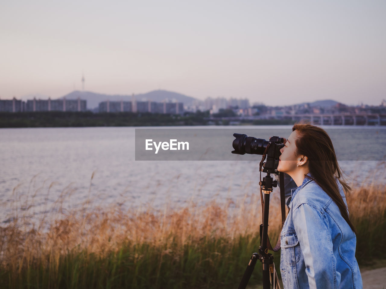 Woman photographing against sky during sunset