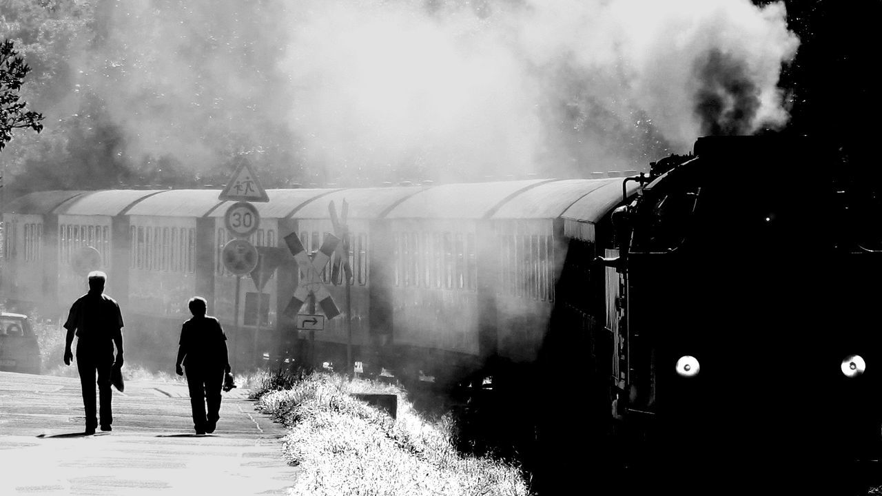 Rear view of couple walking at railroad station platform by steam train