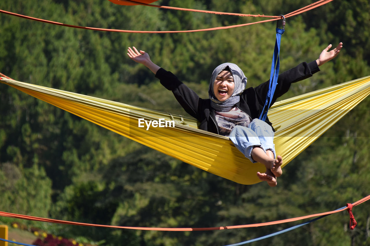 Full length of woman with arms outstretched sitting on hammock