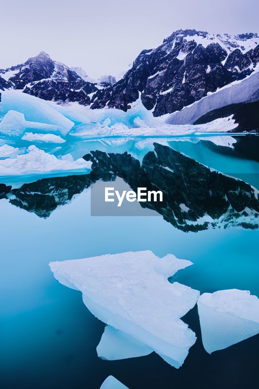 Scenic view of snowcapped mountains against sky with ice floating in the ocean.