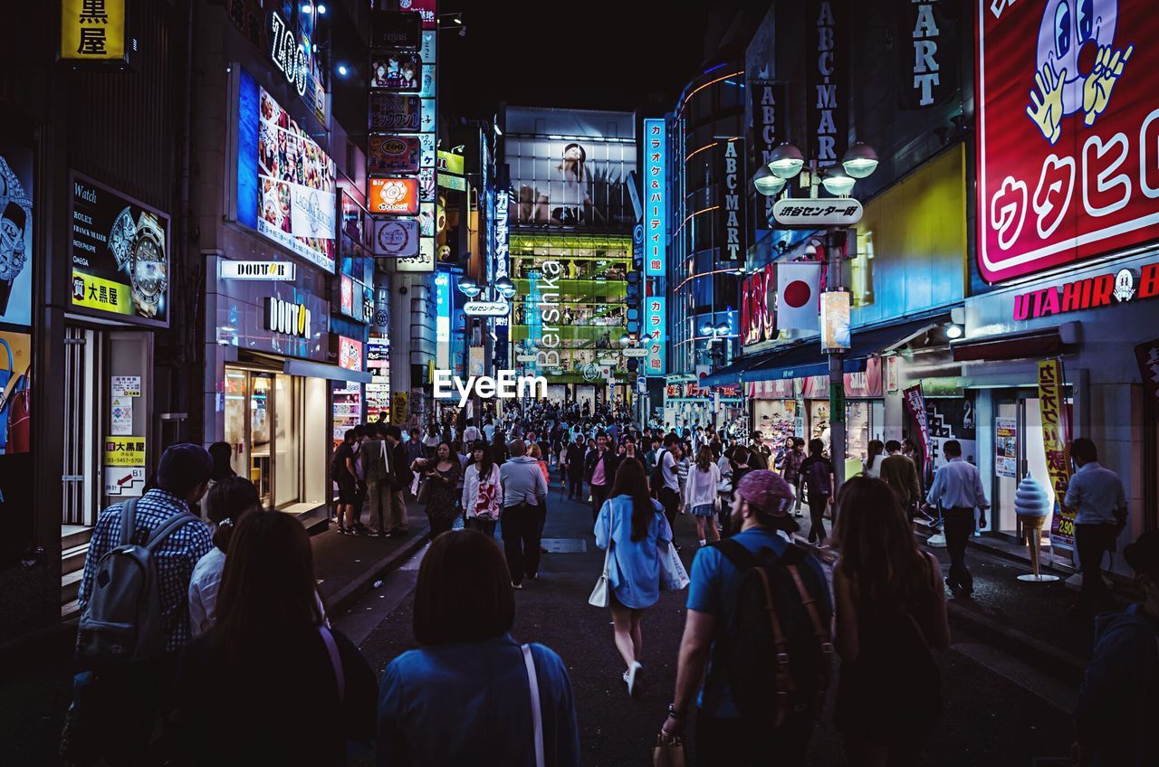 People on road by illuminated buildings at night