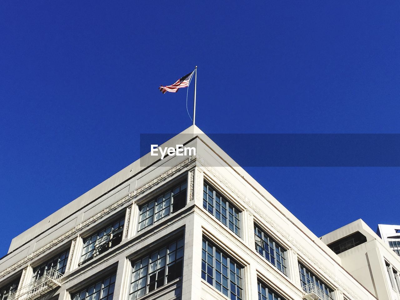 Low angle view of american flag on top of building against clear blue sky