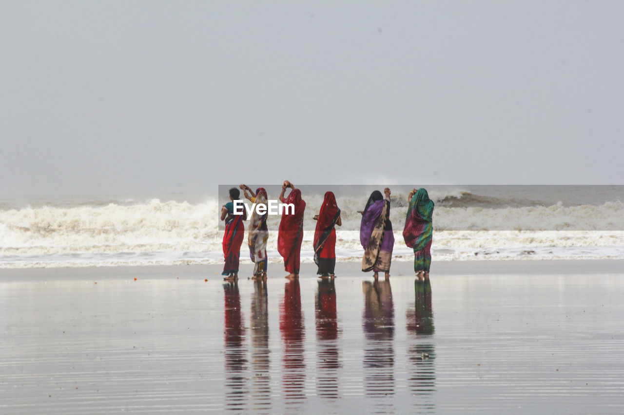 Rear view of women performing rituals while standing on wet shore
