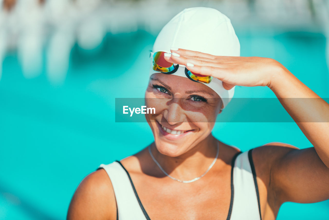 Portrait of a smiling woman shielding eyes while wearing swimming goggles