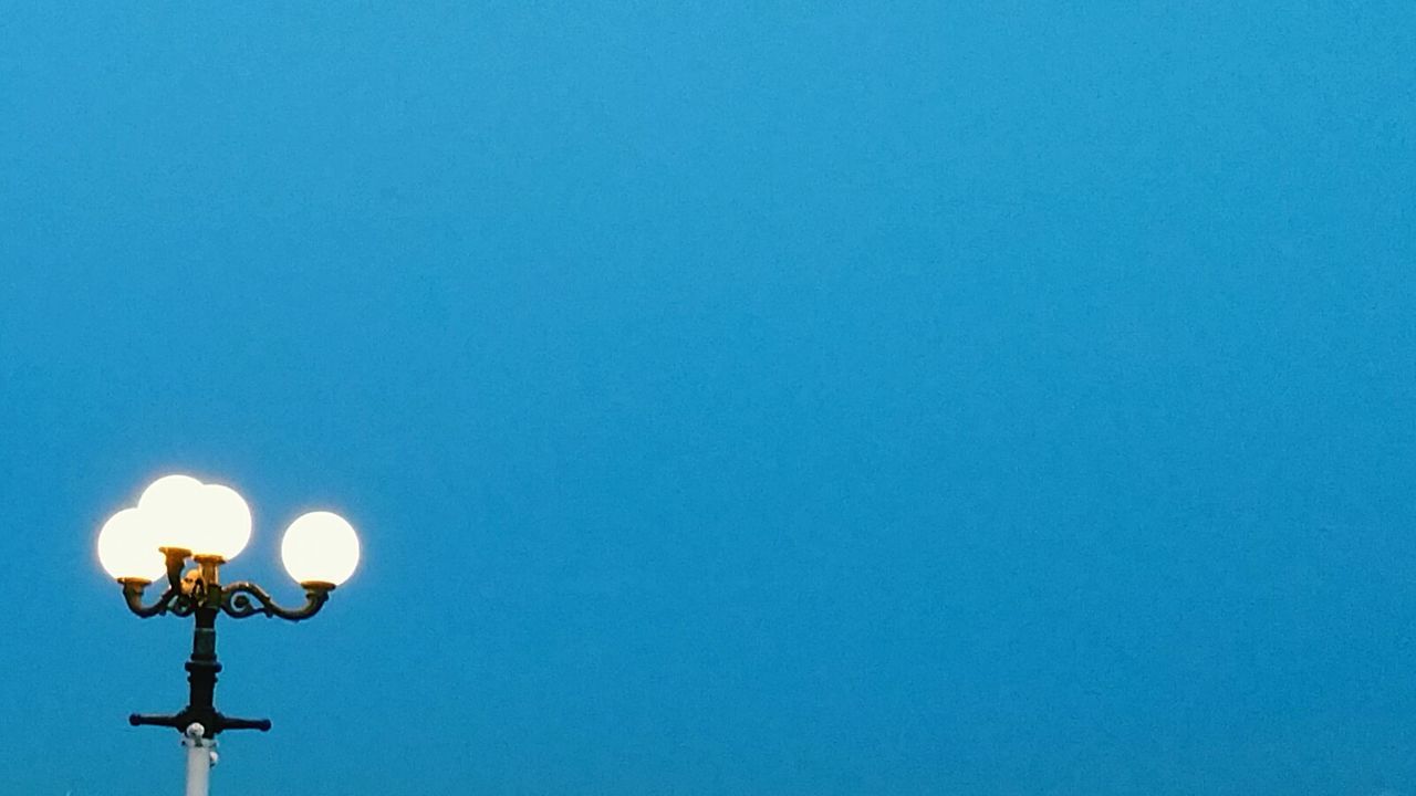 Low angle view of illuminated street light against clear blue sky