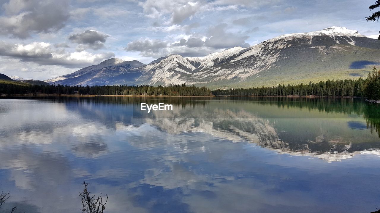 Scenic view of calm lake by mountains against cloudy sky