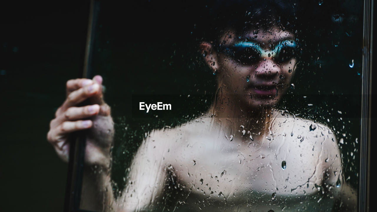 Shirtless young man holding frame while swimming in lake