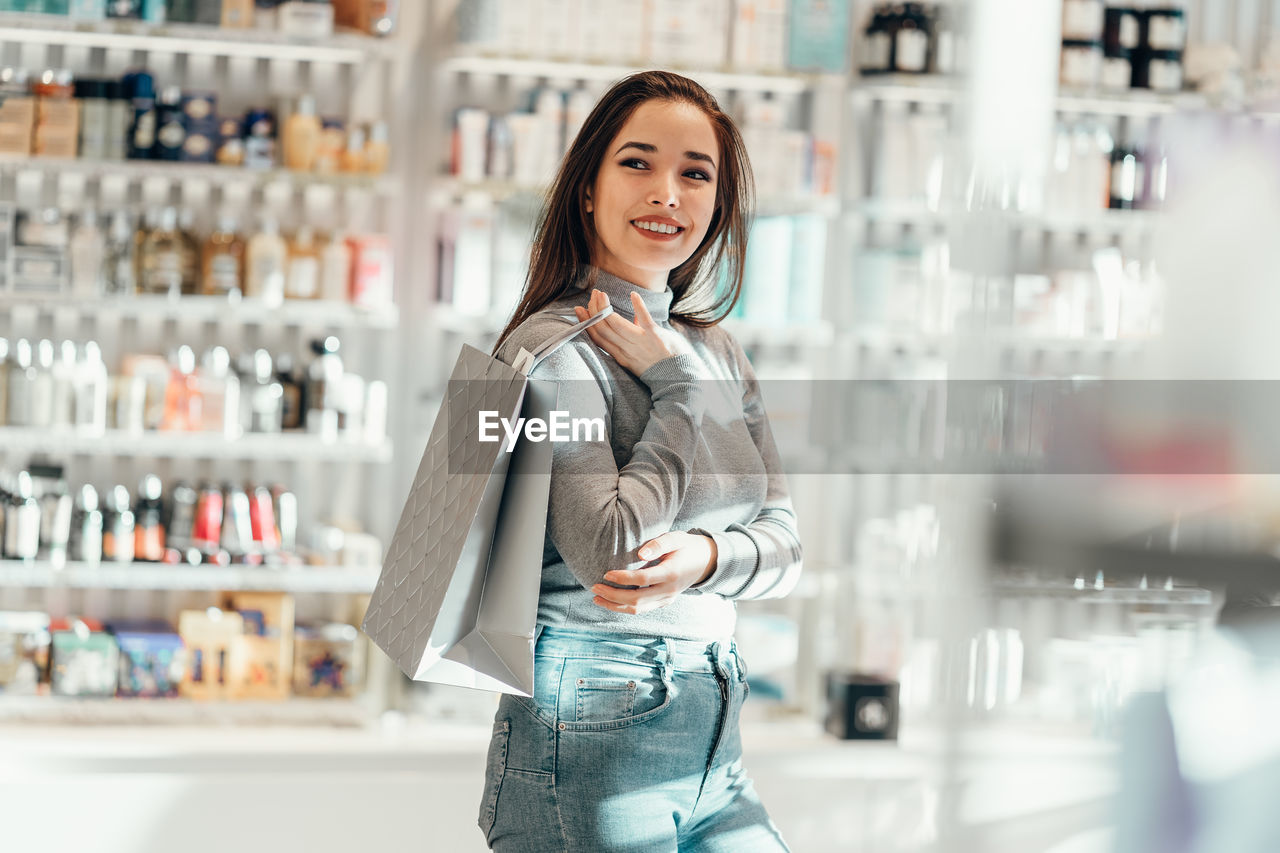 Smiling young woman holding shopping bag at cosmetic store