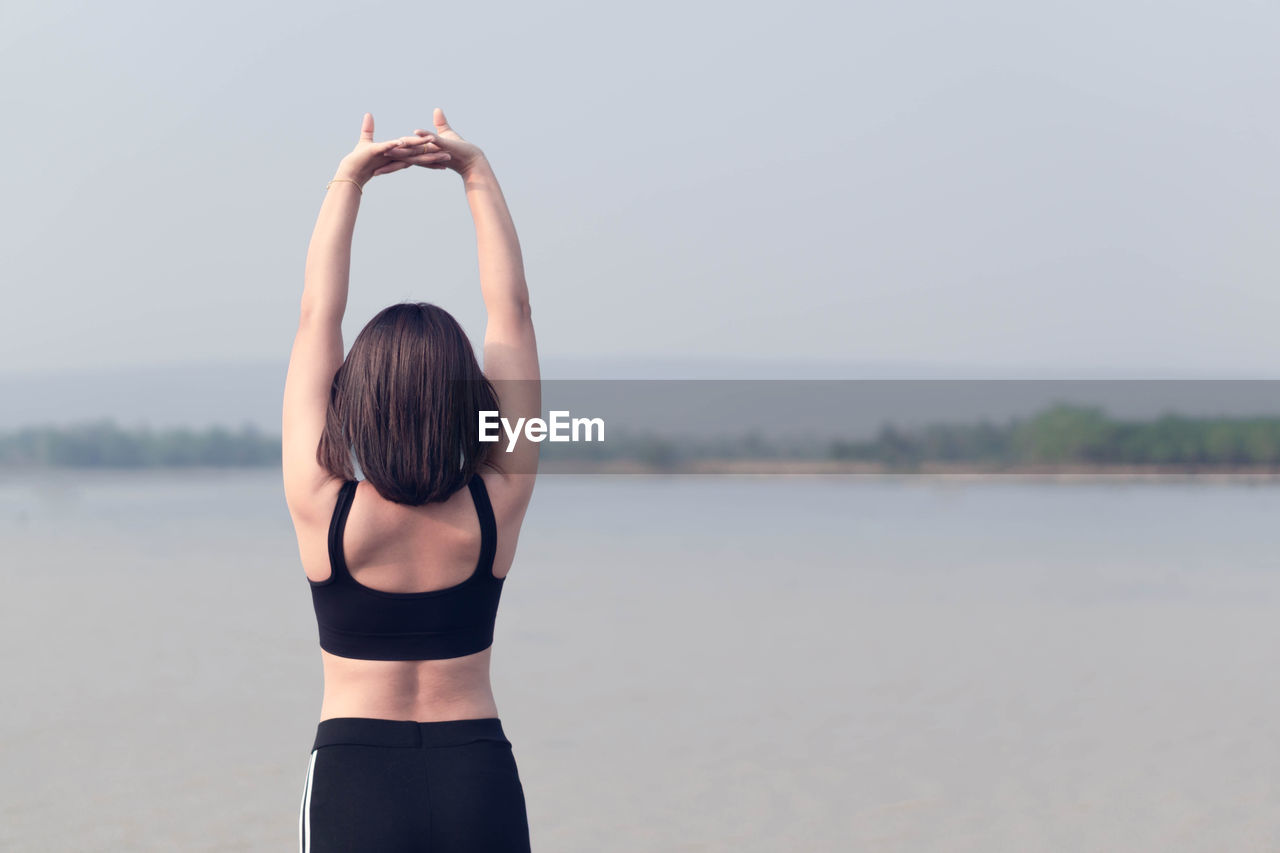 REAR VIEW OF WOMAN WITH ARMS RAISED STANDING IN WATER