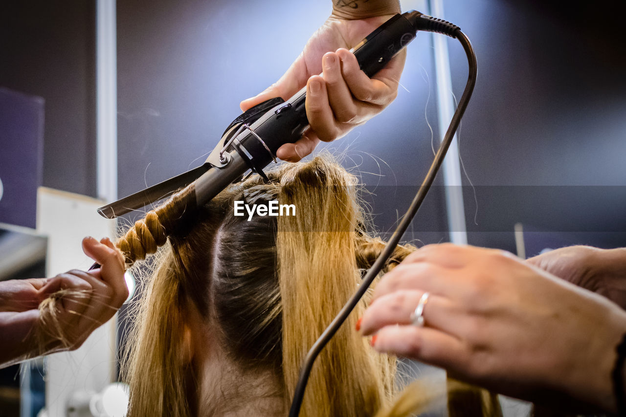 Cropped image of beauticians curling hair in salon