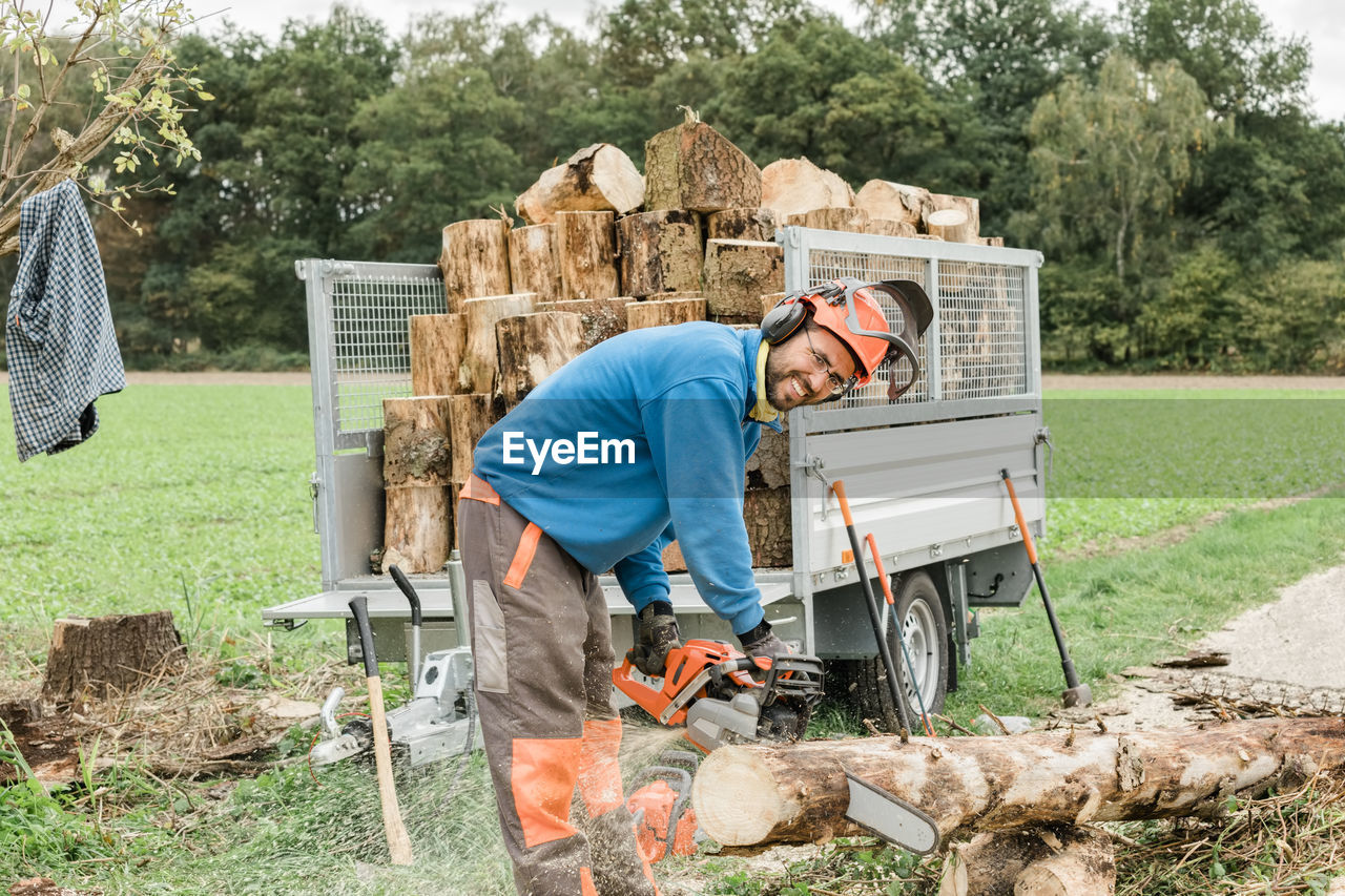 Portrait of smiling worker cutting tree trunk outdoors