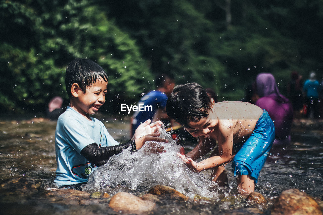 Playful boys splashing water in lake at forest