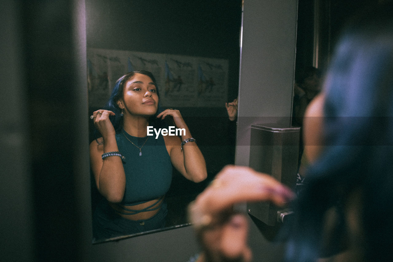 Reflection of young woman looking at mirror reflection in nightclub bathroom