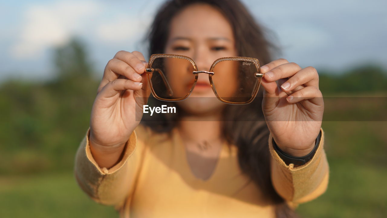 PORTRAIT OF WOMAN WEARING SUNGLASSES HOLDING CAMERA