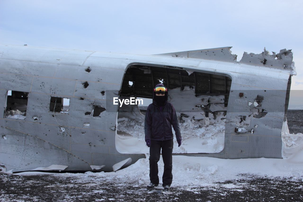 Full length portrait of person standing by damaged airplane at beach during winter
