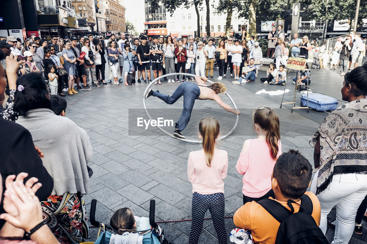 Audience looking at street performer on footpath in city