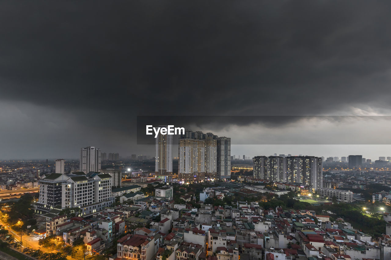 Aerial view of illuminated buildings in city against strom clouds