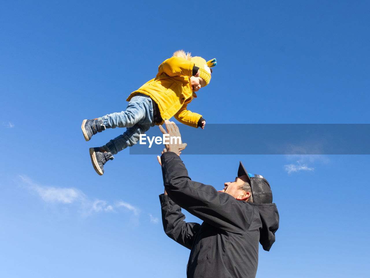 low angle view of man with arms raised against clear blue sky