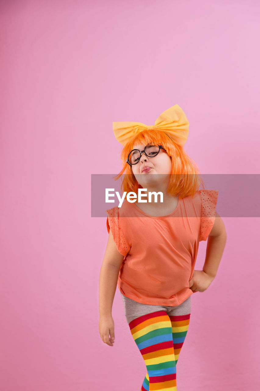 Portrait of cute girl sticking out tongue while standing against pink background