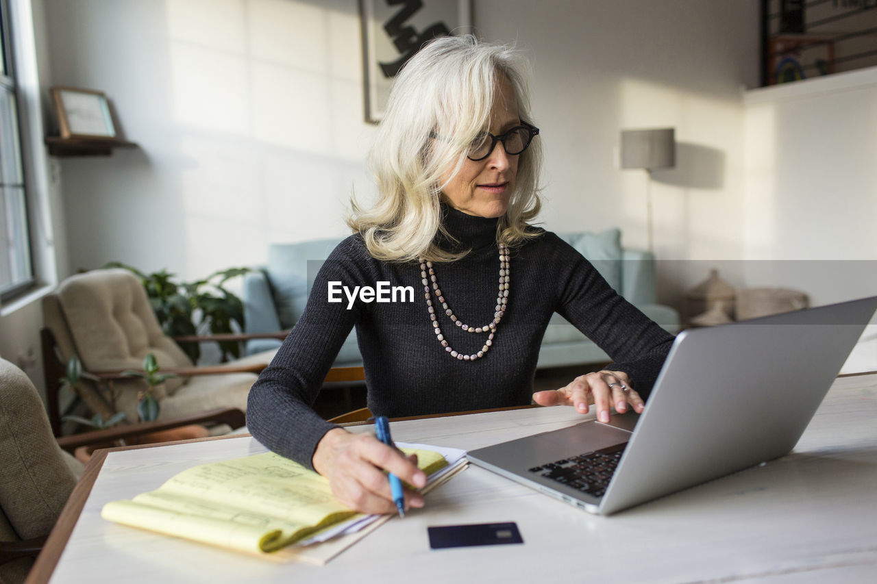 Serious senior woman using laptop computer while paying bills at home