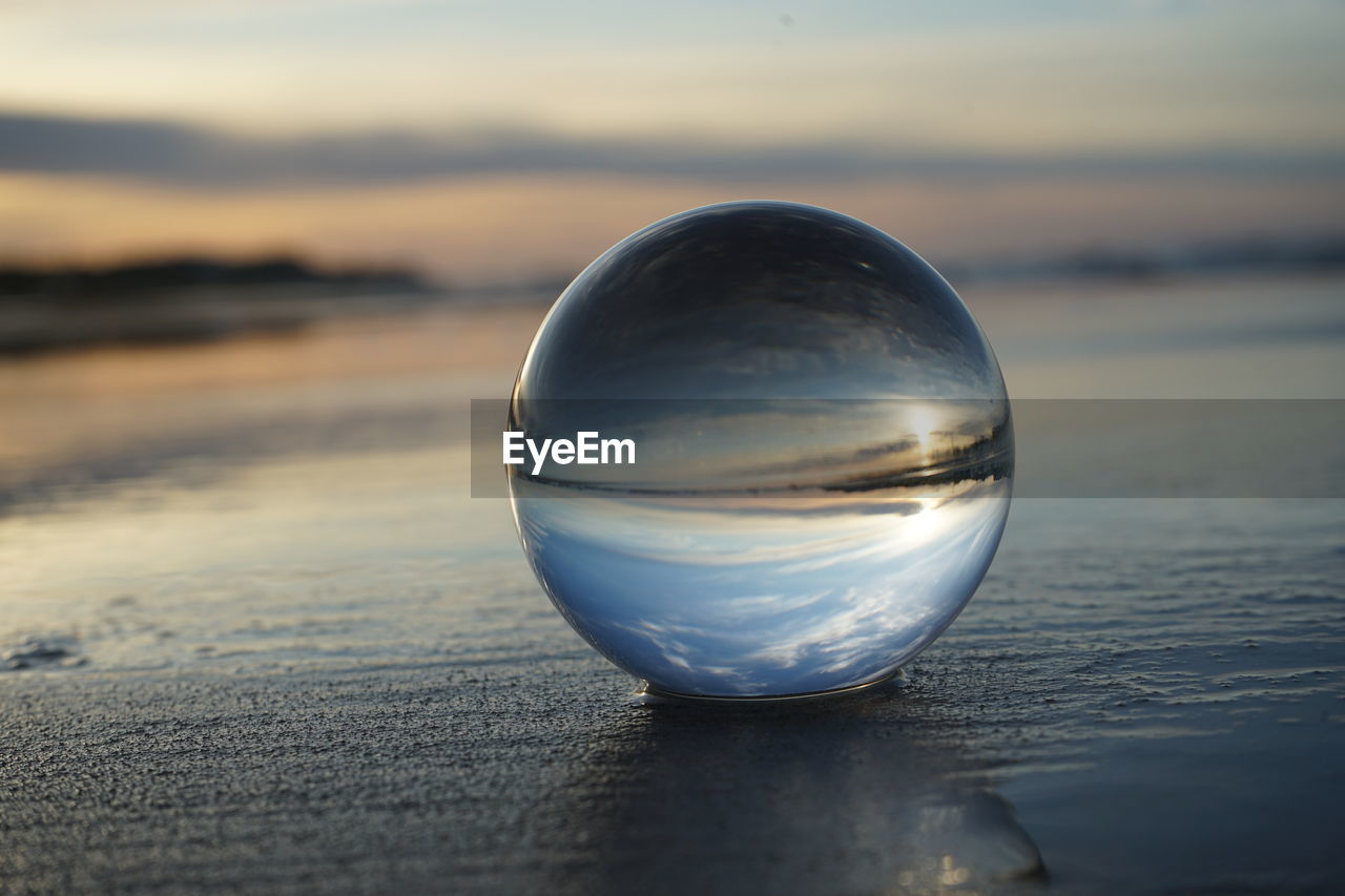 CLOSE-UP OF CRYSTAL BALL ON BEACH AGAINST SKY