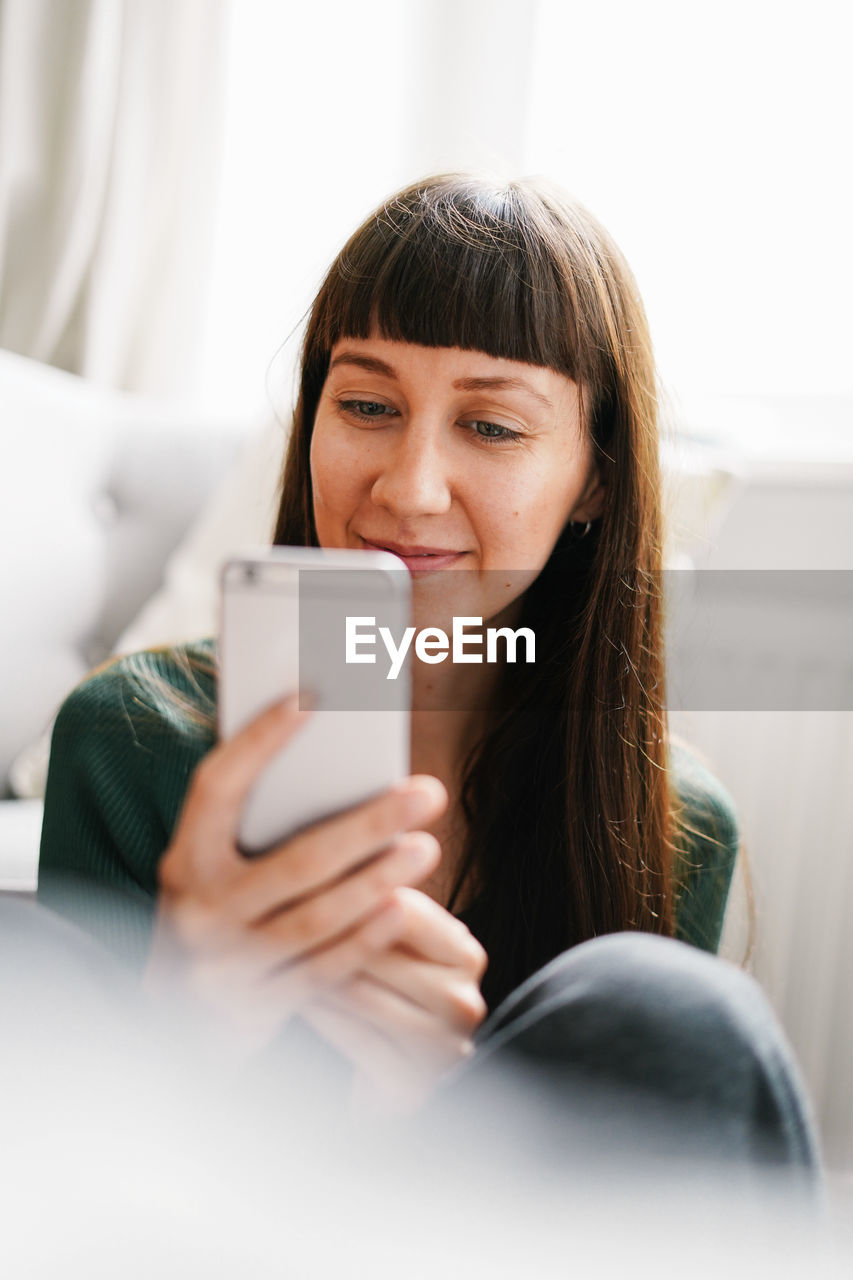 Smiling young woman using mobile phone while sitting at home