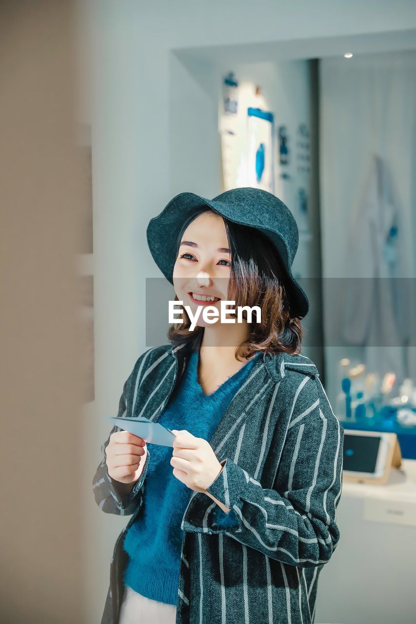 SMILING YOUNG WOMAN USING PHONE WHILE STANDING ON MIRROR