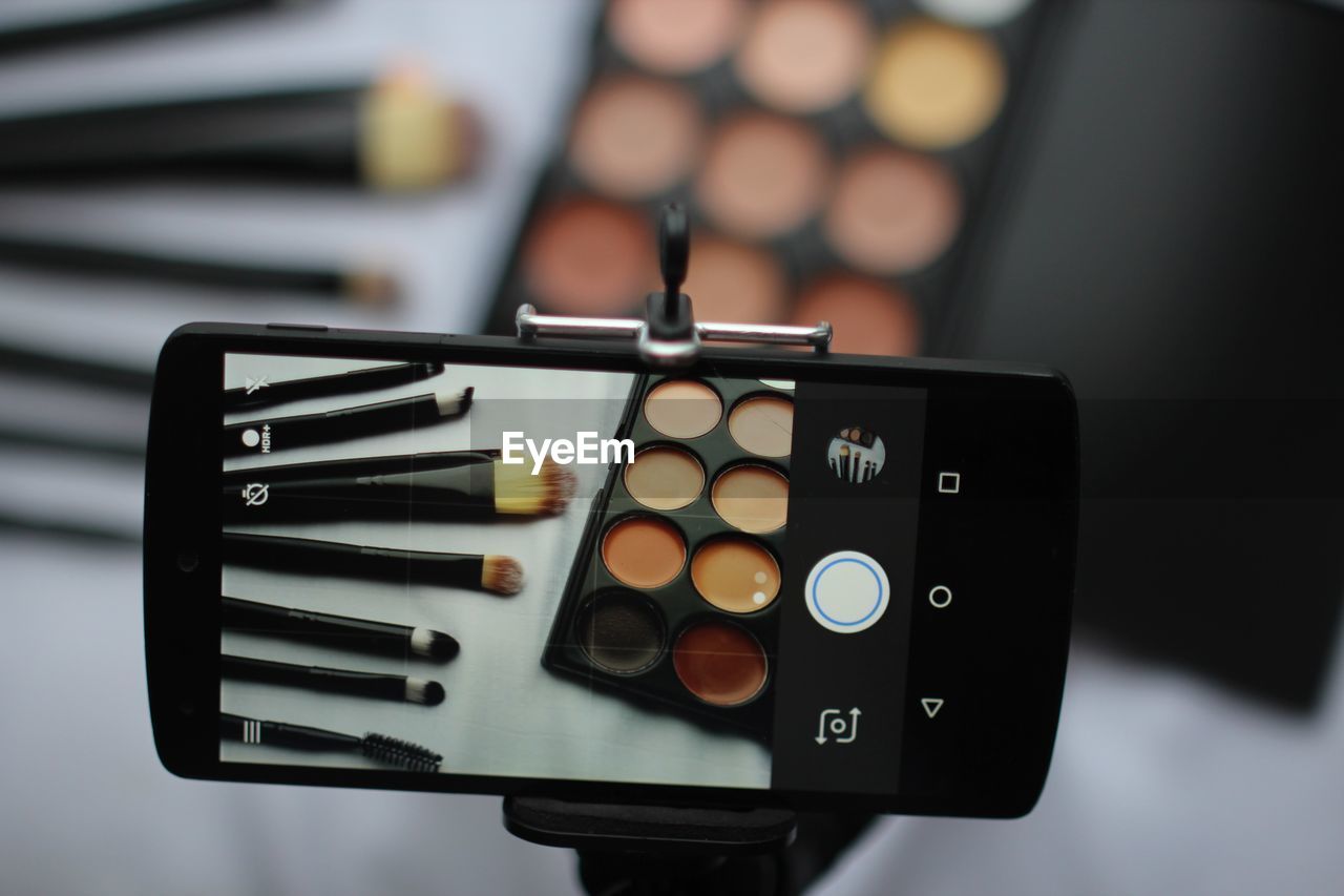 Close-up of smart phone photographing make-up on table