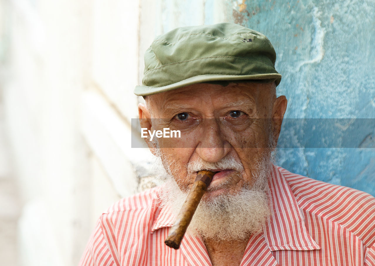 Portrait of senior man wearing cap smoking cigar while sitting outdoors