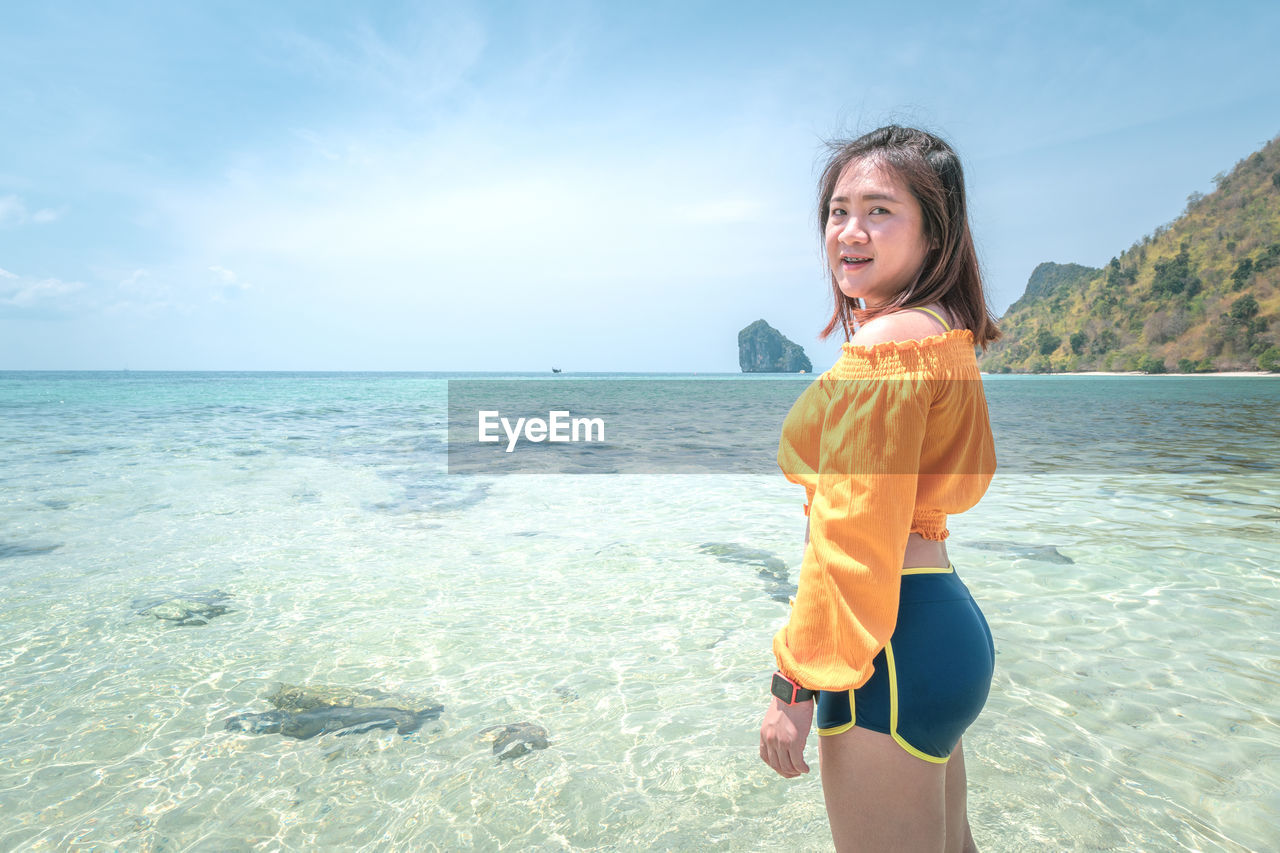 Portrait of smiling woman standing at beach against sky