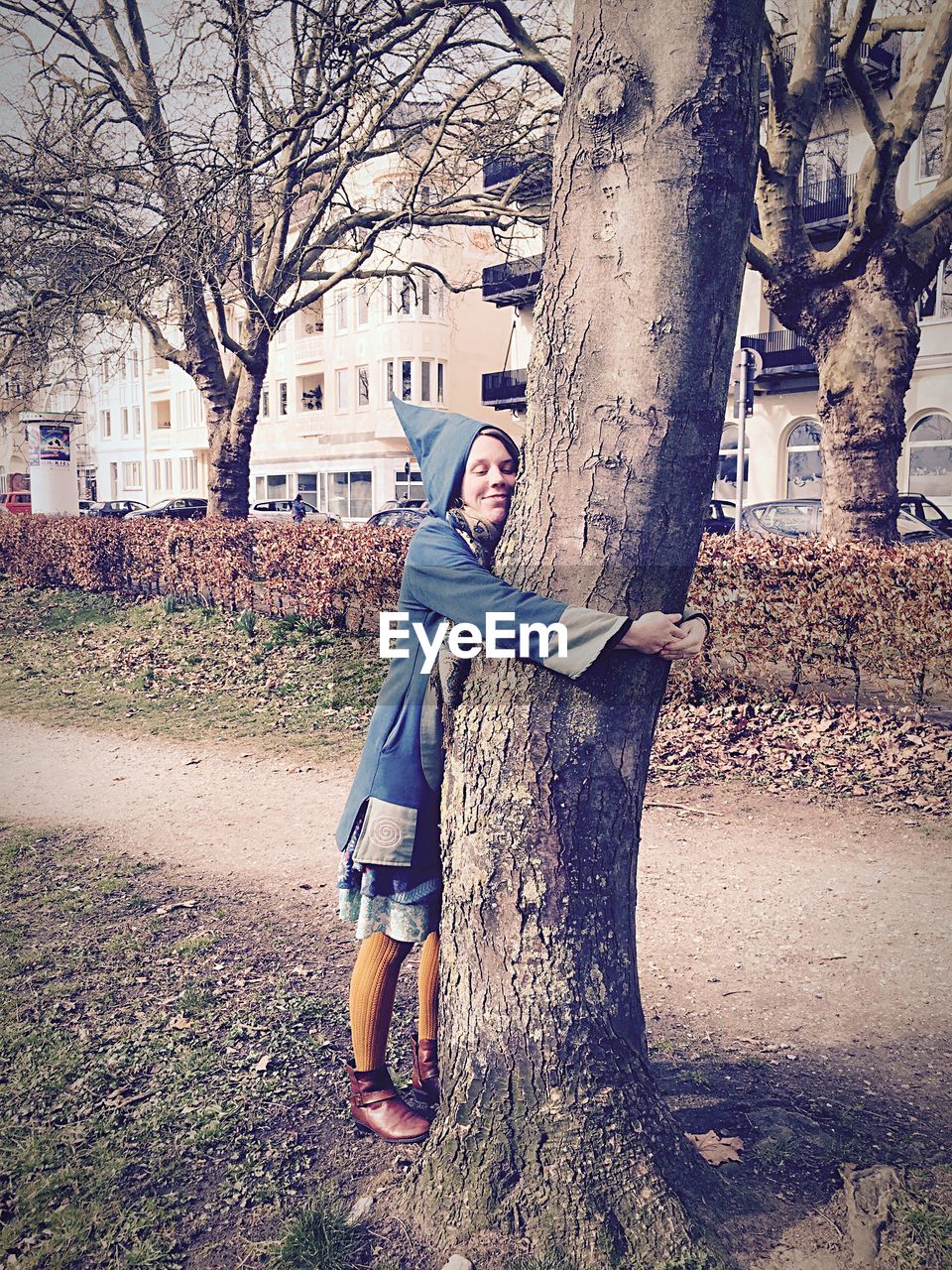 Full length of woman embracing while standing by tree trunk