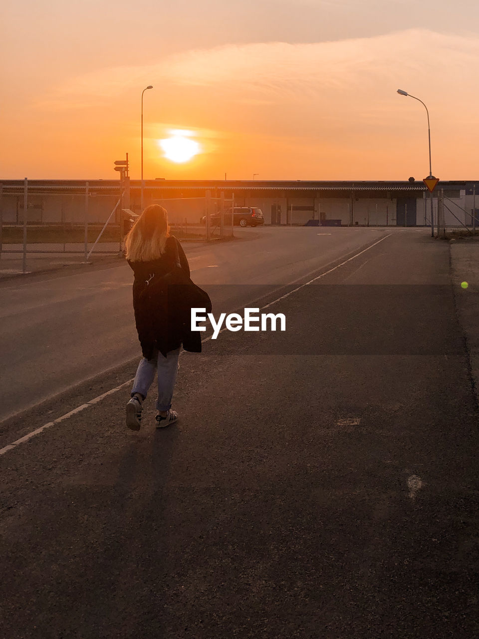 REAR VIEW OF WOMAN ON STREET DURING SUNSET