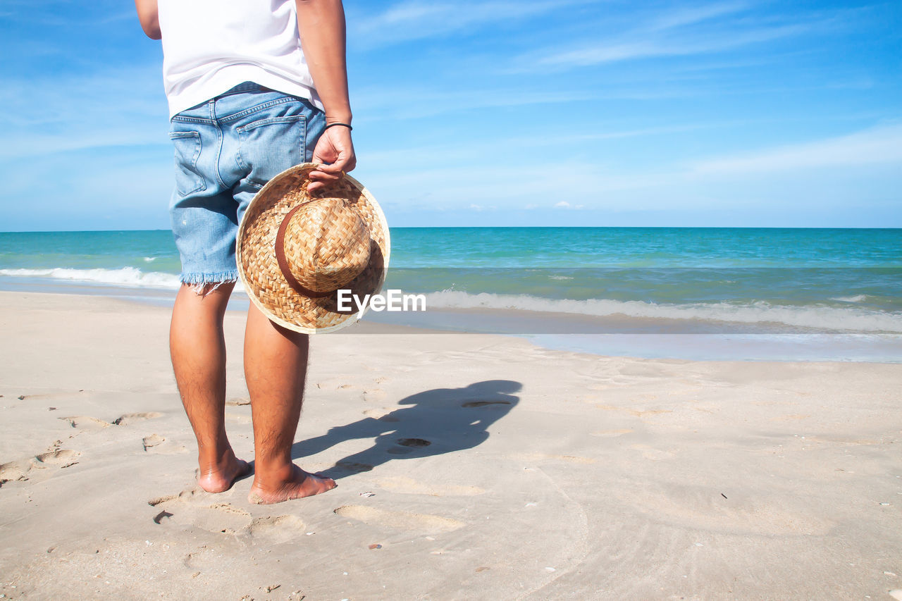 Low section of man standing at beach against sky